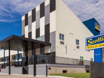 Hotel entrance with canopy, two story building with covered walkways , exterior guest room entrances and stairways, parking spaces, brand signage