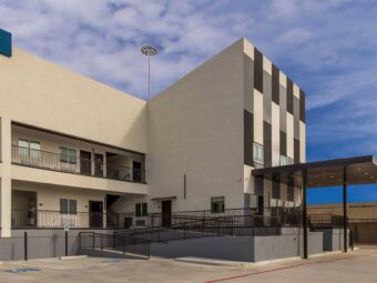 Hotel entrance with canopy, two story building with covered walkways , exterior guest room entrances and stairways, parking spaces