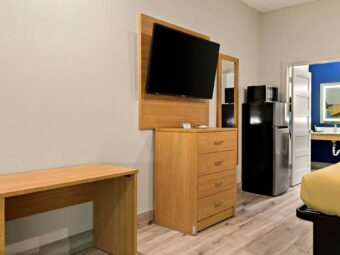 Desk, wooden drawer unit, wall mounted TV, full length mirror, full size fridge with microwave, doorway to bathroom, laminate flooring