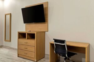 Full length mirror, wooden drawer unit, wall mounted TV, desk with office chair, tiled flooring