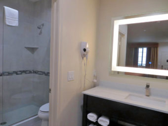 Vanity unit, wall mounted hairdryer, illuminated mirror, doorway to bathroom with shower and toilet