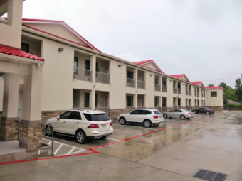 Two story building with exterior room entrances and covered walkways, parking spaces