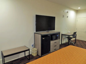 king bed, occasional table, wooden unit with fridge, microwave and flat screen tv, desk with office chair, carpet flooring