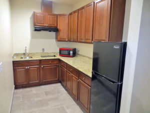 Base and wall cabinets, counter top with sink, hob and microwave, full size fridge, tiled flooring
