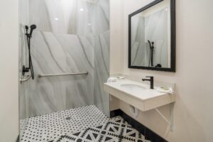 Roll in shower with grab rails, vanity unit with towels, mirror, tiled flooring