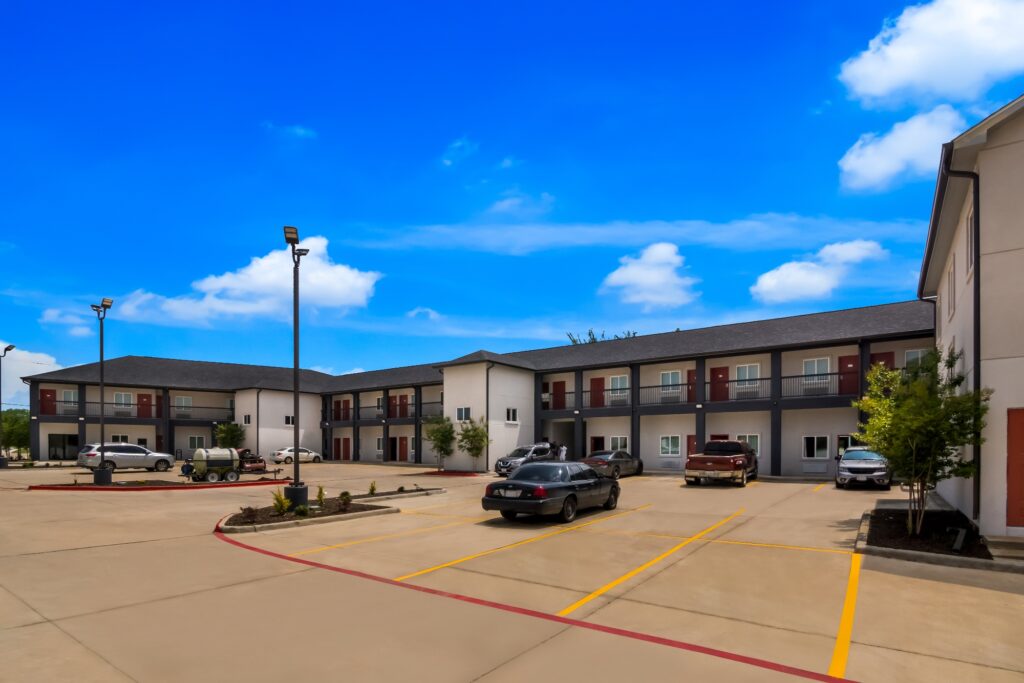 STXFS Exterior 5 Two story building with covered walkways with exterior guest room entrances, parking spaces, landscaped areas with shrubs and small trees