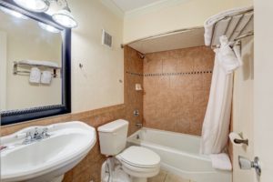 mirror with overhead lighting, sink, toilet, shower tub, shower curtain, towel shelf with towels, tiled flooring