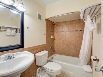 mirror with overhead lighting, sink, toilet, shower tub, shower curtain, towel shelf with towels, tiled flooring
