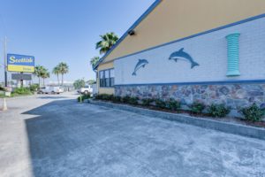 Brand signage, hotel entrance, palm trees, parking spaces