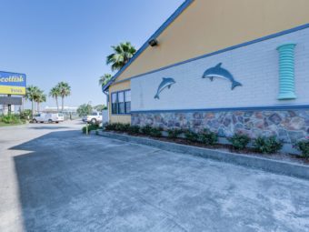 Brand signage, hotel entrance, palm trees, parking spaces