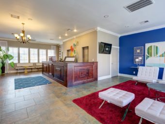 Guest check in desk, bench seating with yellow occasional table, white easy chairs and stoold, occasional table, wall mounted flat screen tv, art images, tiled flooring with rugs