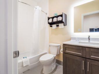 toilet, shower tub with shower curtain, toilet, shelf with towel rail and towels, vanity unit, mirror, tiled flooring