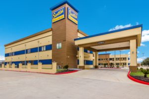 Hotel entrance with canopy drive through, two story building, parking spaces, grassy areas and landscaping