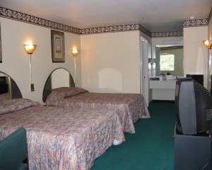 Two double beds, wooden unit with tv, chair, carpet flooring, alcove with vanity unit and mirror