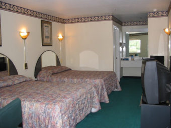 Two double beds, wooden unit with tv, chair, carpet flooring, alcove with vanity unit and mirror