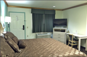 King bed, wall mounted bedside light, corner unit with flat screen tv, desk with chair, carpet flooring