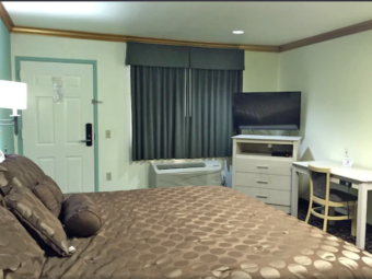 King bed, wall mounted bedside light, corner unit with flat screen tv, desk with chair, carpet flooring