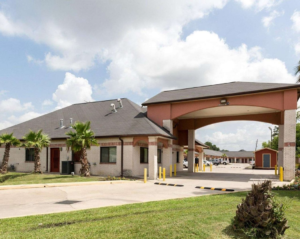 Hotel entrance with drive through canopy, one story building, grassy areas and small palm trees