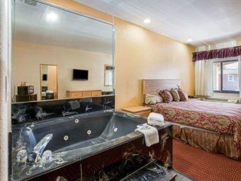 Jacuzzi Tub with towels and bathroom amenities, mirrored walls and tiled surround, night stand, king bed, carpet flooring