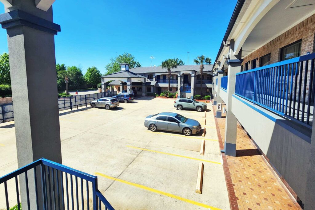 STXHG-Exterior-105 Two story building with exterior guest room entrances, covered walkways and stairs, parking spaces, hotel entrance with drive through canopy