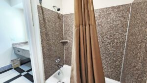 Shower tub with shower curtain, doorway to vanity unit, tiled flooring