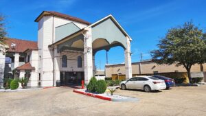 Hotel entrance with drive thru canopy, landscaping with trees and shrubs, parking area