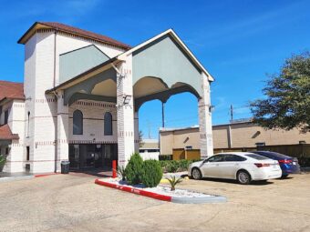 Hotel entrance with drive thru canopy, landscaping with trees and shrubs, parking area