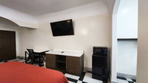 King bed, desk with chair, storage unit, wall mounted TV, mini fridge with microwave, tiled flooring