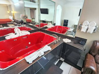 Spa tub with tiled surround and mirrored walls, towel rack with towels, sofa, tiled flooring