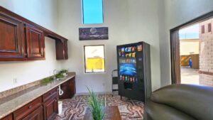 Counter with sink, vending machine with snacks and soda, sofa, coffee table with plant, tiled flooring