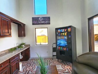 Counter with sink, vending machine with snacks and soda, sofa, coffee table with plant, tiled flooring