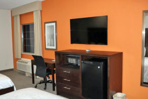 Desk with office chair, art image and flat screen tv, wooden unit with microwave and fridge, two queen beds
