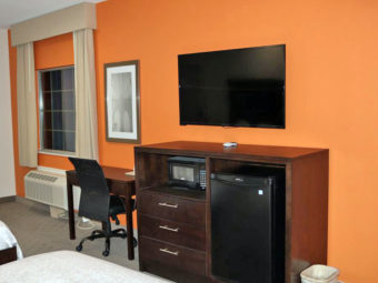 Desk with office chair, art image and flat screen tv, wooden unit with microwave and fridge, two queen beds