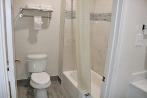 Shower tub with shower curtain, toilet, towel rail and shelf with towels, tiled flooring