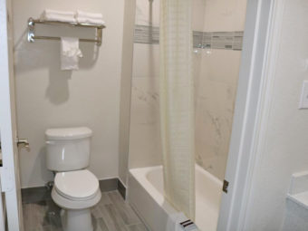 Shower tub with shower curtain, toilet, towel rail and shelf with towels, tiled flooring