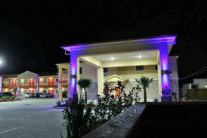 Hotel entrance with night lighting and canopied drive through, two story building with exterior room entrances, covered walkways, parking spaces