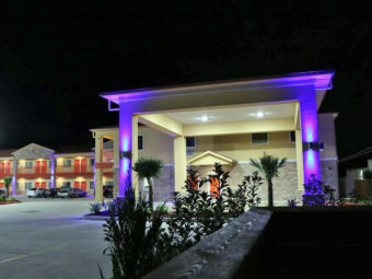 Hotel entrance with night lighting and canopied drive through, two story building with exterior room entrances, covered walkways, parking spaces
