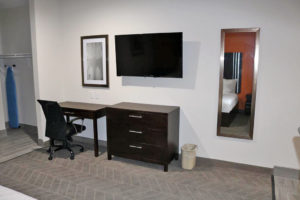 Desk with office chair, wooden drawer unit, wall mounted flat sceeen tv, mirror and art, alcove with hanging rail and ironing board
