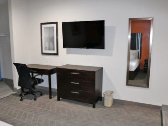 Desk with office chair, wooden drawer unit, wall mounted flat sceeen tv, mirror and art, alcove with hanging rail and ironing board