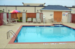 Exterior pool, concrete poolside with patio table, umbrella, chairs and loungers