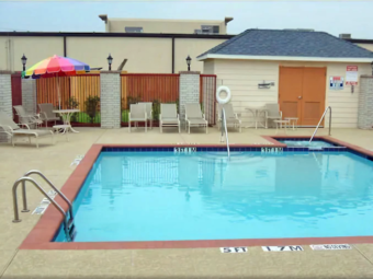 Exterior pool, concrete poolside with patio table, umbrella, chairs and loungers