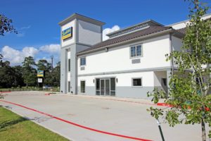 Two story building with hotel entrance, brand signage, grassy areas with small trees