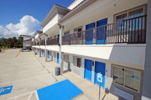 Two story building with exterior room entrances with covered walkways and stairs, parking spaces