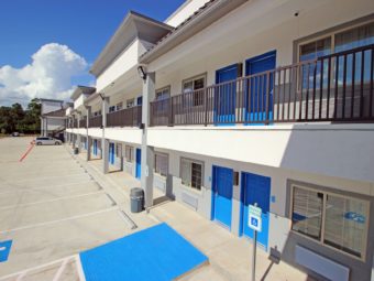 Two story building with exterior room entrances with covered walkways and stairs, parking spaces