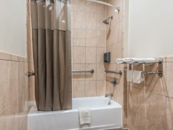 Shower tub with shower curtain, soap dispensers and wall grab bars, low level towel rail and shelf with towels