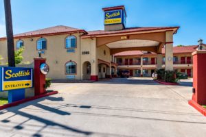 Drive in hotel entrance with canopy with small bushes, two story building and parking spaces