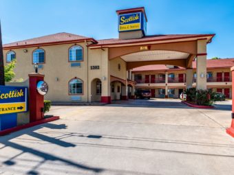 Drive in hotel entrance with canopy with small bushes, two story building and parking spaces