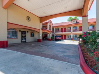 Hotel canopy entrance, two story building, with exterior walkways to room entrances, small flowwwering bushes and parking spaces