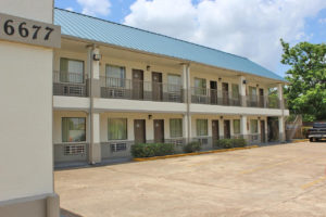 Two story building, exterior entrances to rooms with covered walkways and stairs, parking spaces