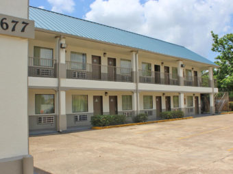 Two story building, exterior entrances to rooms with covered walkways and stairs, parking spaces